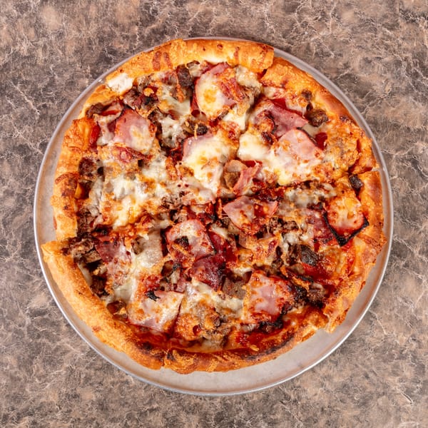 Overhead view of a Mr. G's Pizzeria meat lover's pizza with ham, bacon, and ground beef.