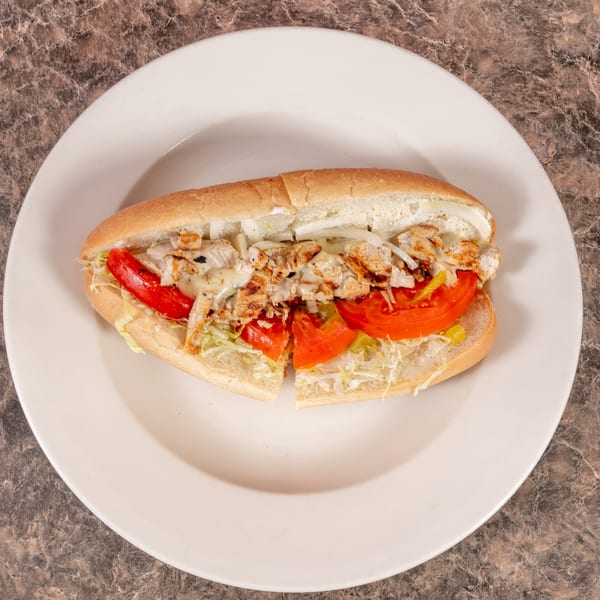 Grilled chicken sub with melted cheese, tomatoes, onions, and lettuce on a white plate.