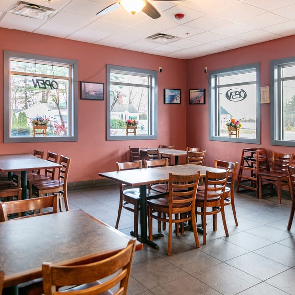 Empty dining room at Mr. G's Pizzeria with wooden tables and chairs, and windows showing an "OPEN" sign.