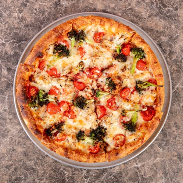 A Mr. G's Pizzeria pizza with melted cheese, cherry tomatoes, and broccoli florets on a metal pan.