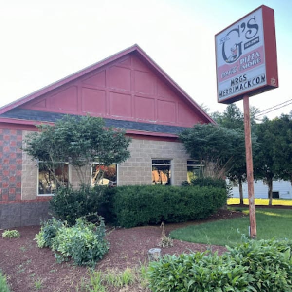 Exterior of Mr. G's Pizzeria, a red and brick building with a tall sign, surrounded by green landscaping.