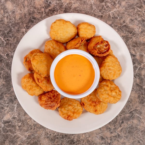 A white plate filled with golden-brown fried mushrooms and a small cup of orange dipping sauce.
