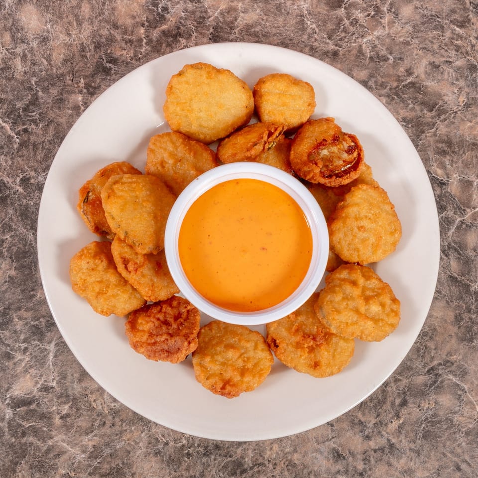 A white plate filled with golden-brown fried mushrooms and a small cup of orange dipping sauce.